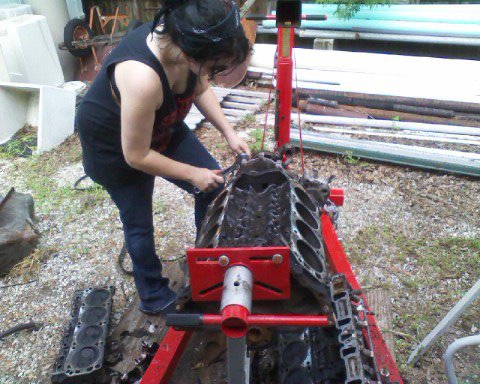 1988 Ford Bronco - A person works on a disassembled engine block mounted on a red engine stand in an outdoor setting.