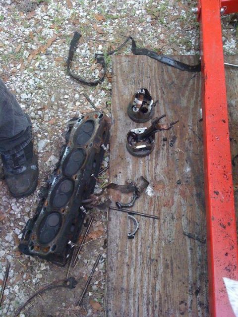 1988 Ford Bronco - Disassembled engine components, including a cylinder head and pistons, are laid out on a wooden surface next to a red engine hoist.