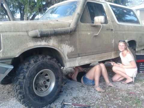 1988 Ford Bronco - Two people work on a muddy Ford Bronco, one person is underneath the vehicle.