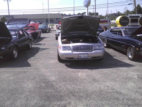 2003 Ford Crown Victoria - A silver 2003 Ford Crown Victoria is parked with its hood open, alongside other vehicles.