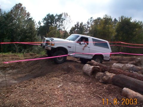 1992 Ford Bronco - A white 1992 Ford Bronco navigates an off-road course marked with pink tape and logs.