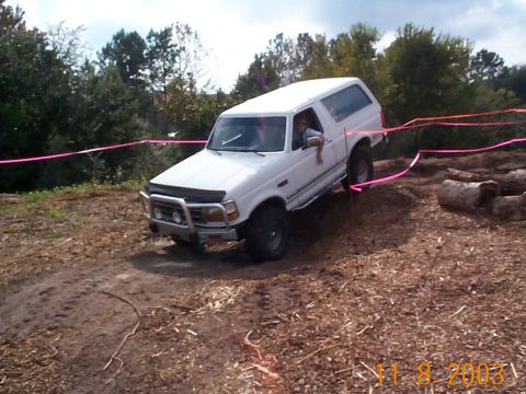 1992 Ford Bronco - A white 1992 Ford Bronco is shown tackling an off-road obstacle course with pink tape marking the path.