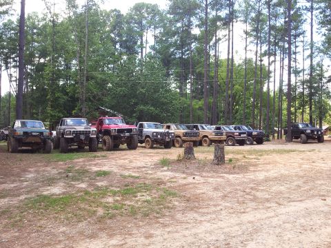 2012 Ford Bronco - A collection of off-road vehicles are lined up in a dirt lot with trees in the background.