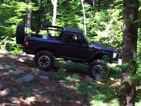 2012 Ford Bronco - Off-road SUV navigates a challenging dirt path surrounded by dense forest foliage.