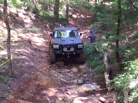 2012 Ford Bronco - An SUV carefully maneuvers through a challenging off-road course with rocky obstacles and dense foliage.