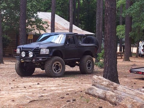 2012 Ford Bronco - Modified black Ford Bronco with large tires and off-road accessories in a natural setting.