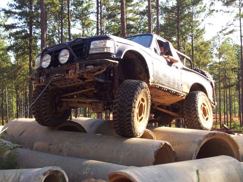 2012 Ford Bronco - Modified black truck navigates an obstacle course of large concrete pipes in a wooded area.
