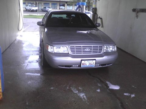 2003 Ford Crown Victoria - A silver 2003 Ford Crown Victoria is parked head-on in a car wash bay, its front grille and license plate clearly visible.