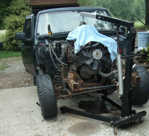 1995 Ford Bronco - Engine bay of a dark green Ford Bronco, with the engine being lifted out by an engine crane.