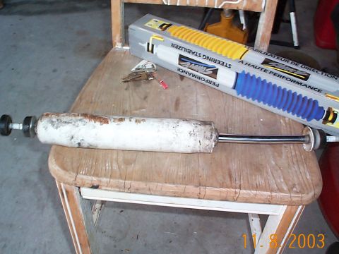 1992 Ford Bronco - A worn steering stabilizer sits on a chair next to a new one in its packaging.