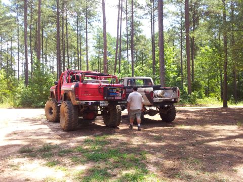 2012 Ford Bronco - Two custom off-road trucks are parked side-by-side in a forest clearing.