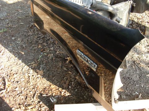 1988 Ford Bronco - A detached black Ford Bronco fender with chrome trim and "Bronco" badging sits beside a radiator.