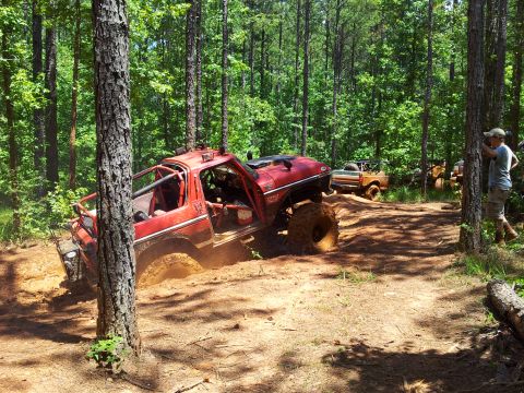 2012 Ford Bronco - Several modified trucks navigate a muddy trail through a forest.