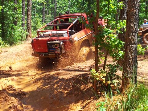 2012 Ford Bronco - A red off-road vehicle navigates a muddy trail, with another vehicle visible in the background.