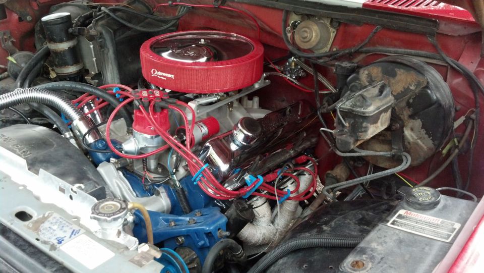 V8 engine bay with red air cleaner cover, red plug wires, chrome valve covers and blue block in a red pickup