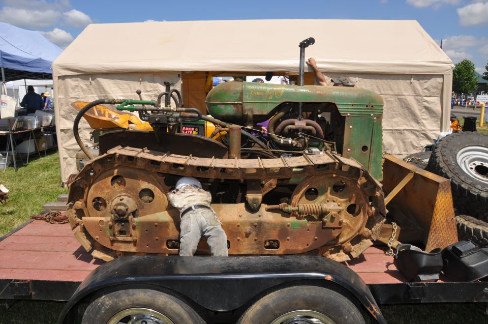 Green crawler tractor with rusty tracks, a person working underneath