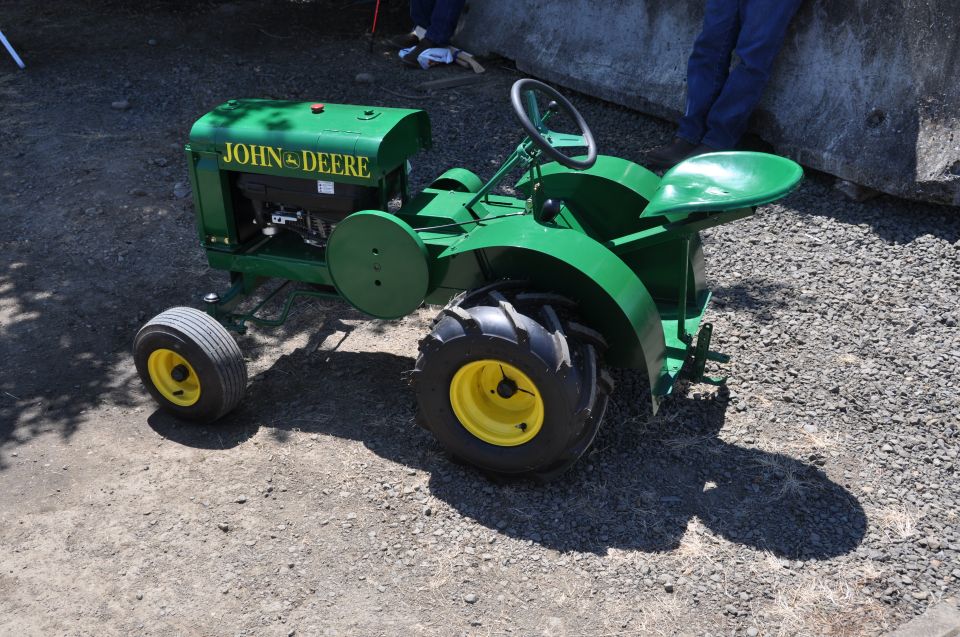 Green John Deere tractor with yellow wheels and black tires, parked on gravel