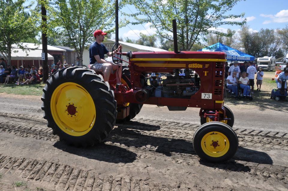 Red Gibson tractor with yellow wheels and number 73 on the side, driven by a man in a red hat