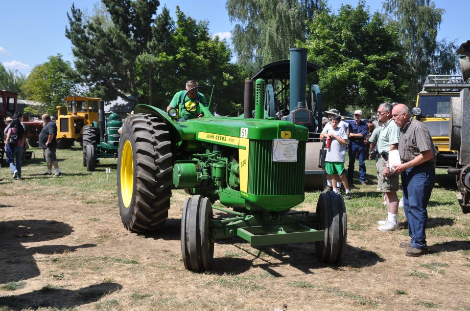 John Deere 4020 tractor with a man driving, parked outdoors at a show with other tractors and people