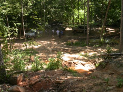 1990 Ford Bronco - A group of people and off-road vehicles gather in a wooded area, possibly for an outdoor event or trail ride.