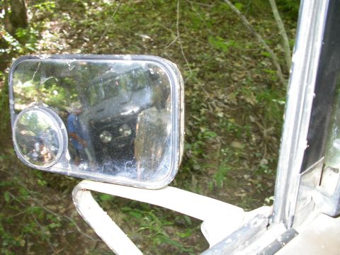 1990 Ford Bronco - Reflection of a dark SUV with round headlights is visible in the dirty side mirror of another vehicle.