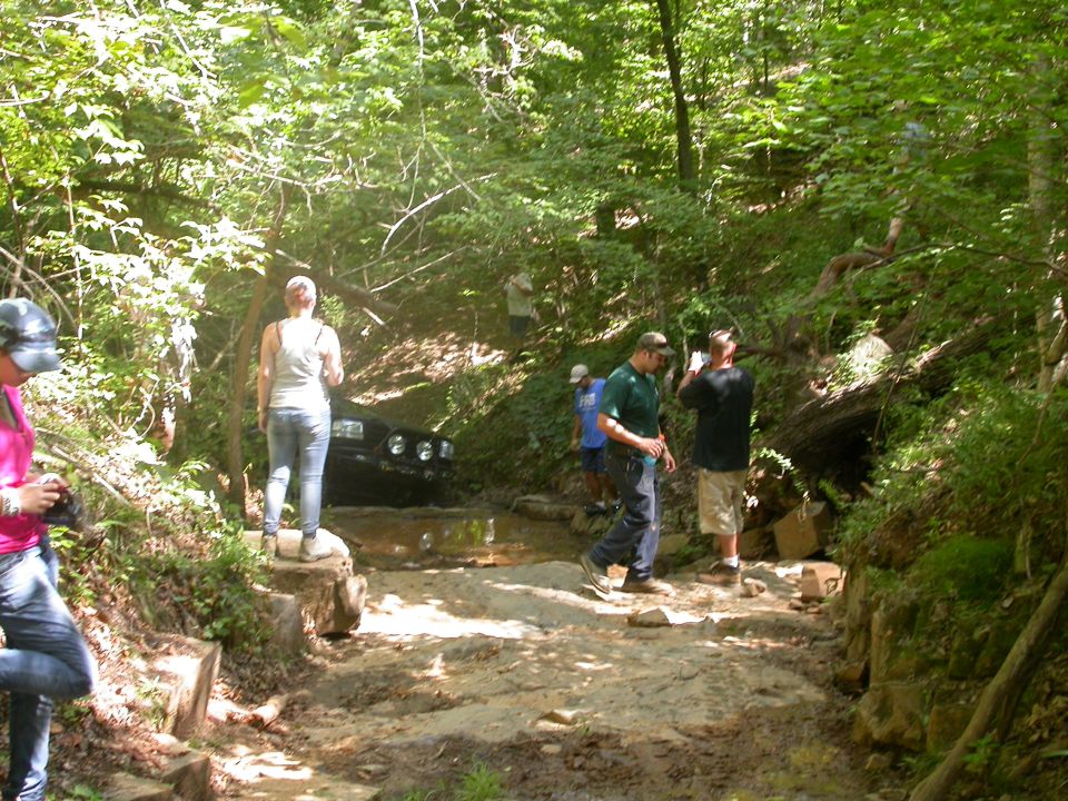 1990 Ford Bronco navigating a muddy off-road trail with people watching