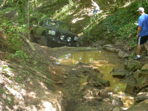 1990 Ford Bronco - A 1990 Ford Bronco tackles a challenging off-road course with a muddy water crossing.