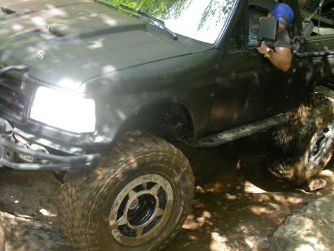 1990 Ford Bronco - A driver navigates a muddy, off-road trail in a modified SUV.
