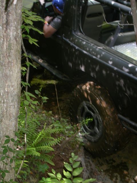 1990 Ford Bronco - An off-road vehicle navigates a challenging, wooded terrain with steep inclines and rocky obstacles.