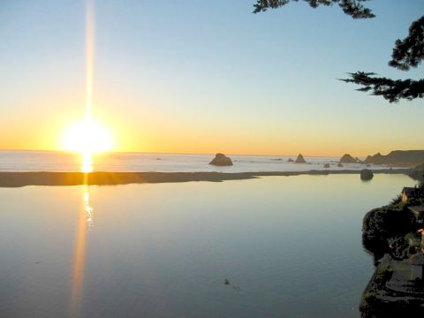 2002 Ford Taurus - A ocean sunset casts a golden glow over calm waters, with rocks dotting the coastline.