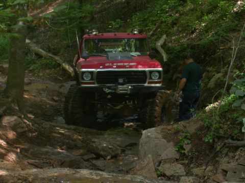 1990 Ford Bronco - A heavily modified red truck drives through a challenging off-road course.