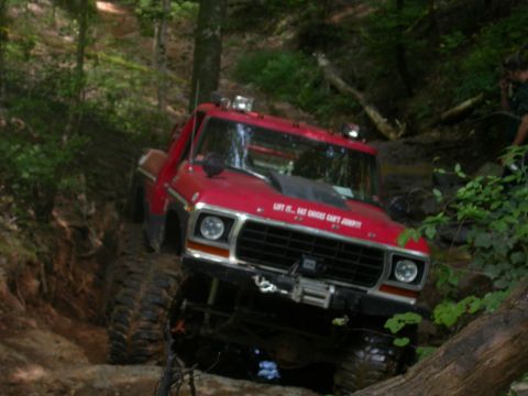 1990 Ford Bronco - This red Ford F-Series truck is tackling a challenging muddy trail with its off-road modifications.