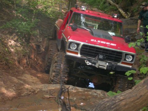 1990 Ford Bronco - This modified truck is tackling a challenging off-road course with deep mud and steep inclines.