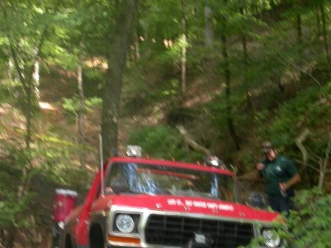 1990 Ford Bronco - A red truck navigates a wooded trail, with a person observing from the side.