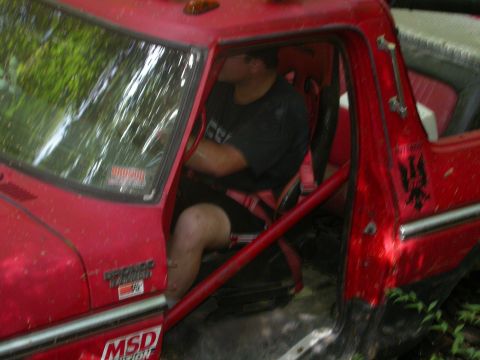 1990 Ford Bronco - Driver sits in a red off-road vehicle, modified with a roll cage and racing seat, ready for action.