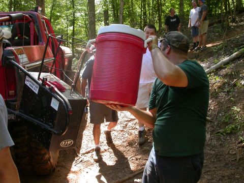 1990 Ford Bronco - People are gathered around an off-road vehicle, with one person carrying a large cooler.