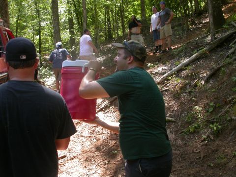 1990 Ford Bronco - A group of people are gathered in a wooded area, with one person carrying a large red cooler.