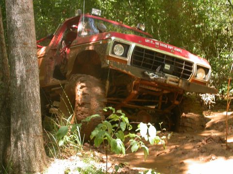 1990 Ford Bronco - This heavily modified off-road vehicle navigates a muddy trail through a wooded area.