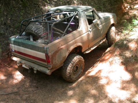 1990 Ford Bronco - This modified Ford Bronco is navigating a challenging off-road trail, covered in mud.