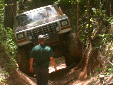 1990 Ford Bronco - A lifted 1979 Ford Bronco navigates a challenging off-road trail, its front end angled upwards on a steep incline.