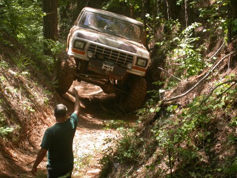 1990 Ford Bronco - A person guides an off-road vehicle as it navigates a challenging trail through a dense forest.