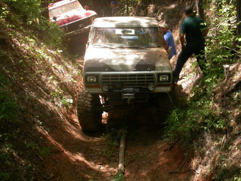 1990 Ford Bronco - Two off-road vehicles navigate a challenging, wooded trail with steep inclines.