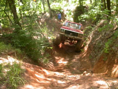 1990 Ford Bronco - Off-road truck navigates a challenging muddy descent on a wooded trail.
