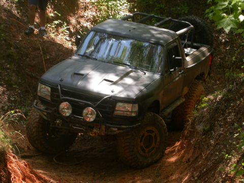 1990 Ford Bronco - This modified truck, likely from the early 1990s, is shown off-roading on a steep, muddy incline.