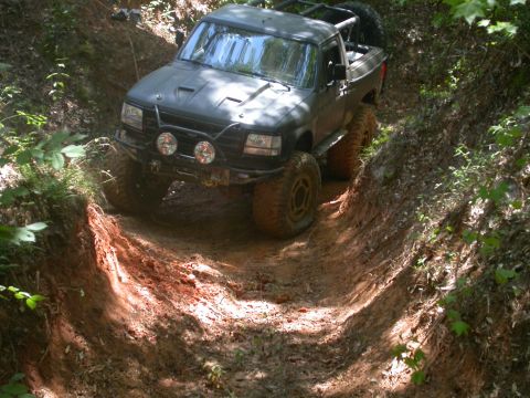 1990 Ford Bronco - Pickup truck with off-road modifications navigating a challenging dirt trail.