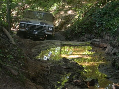 1990 Ford Bronco - This Ford Bronco navigates a challenging muddy off-road course, splashing through a water obstacle.