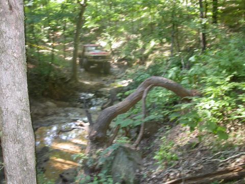 1990 Ford Bronco - Off-road vehicle driving through a wooded stream.