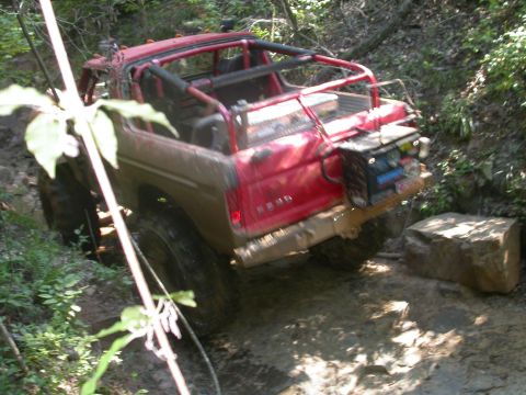 1990 Ford Bronco - Off-road vehicle with roll cage on a muddy trail, possibly a Ford Bronco from the 1980s.