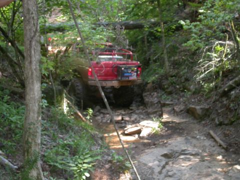 1990 Ford Bronco - This red 1990 Ford Bronco tackles a challenging off-road trail with rocky terrain and a stream crossing.
