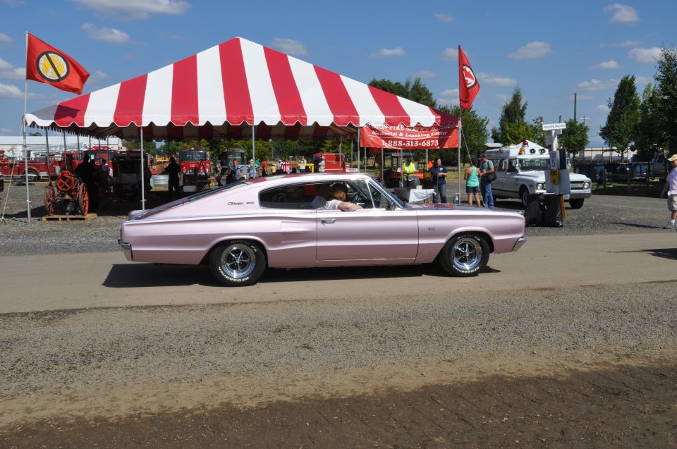 Pink 1966 Dodge Charger parked at an outdoor event with a red and white striped tent in the background